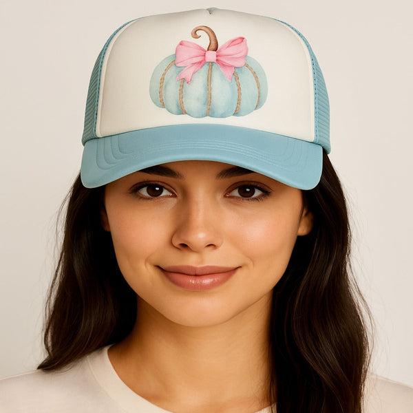 Woman wearing a cap with a pumpkin design and pink bow on a plain background