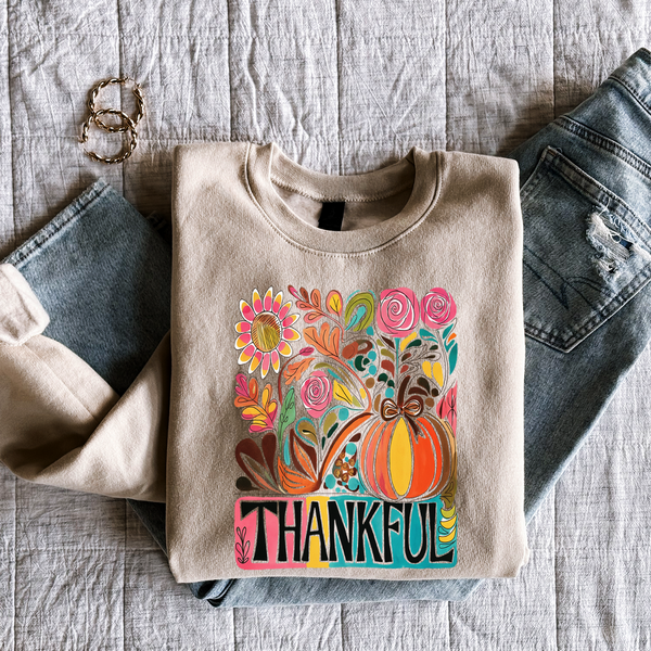 Beige sweatshirt with colorful pumpkin design and 'Thankful' text, placed on a unisex sand color Gildan sweatshirt