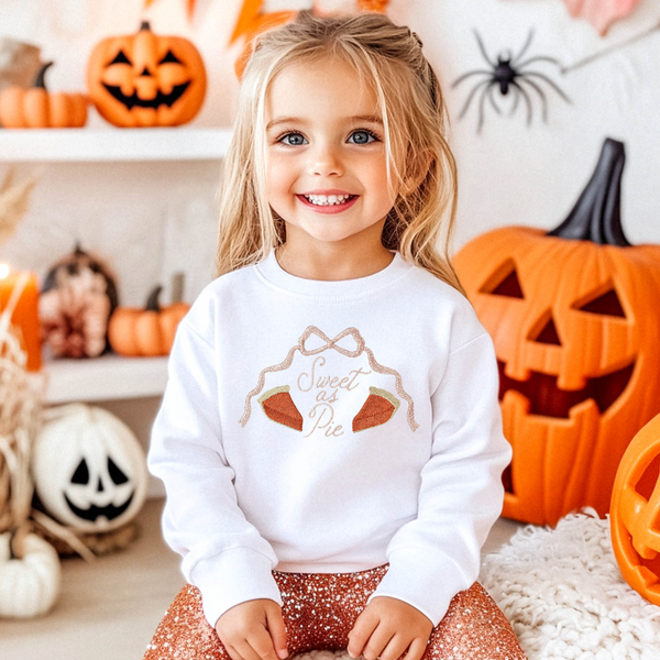 Toddler girl wearing a white sweatshirt embroidered with sweet as pie and two pumpkin pie slices